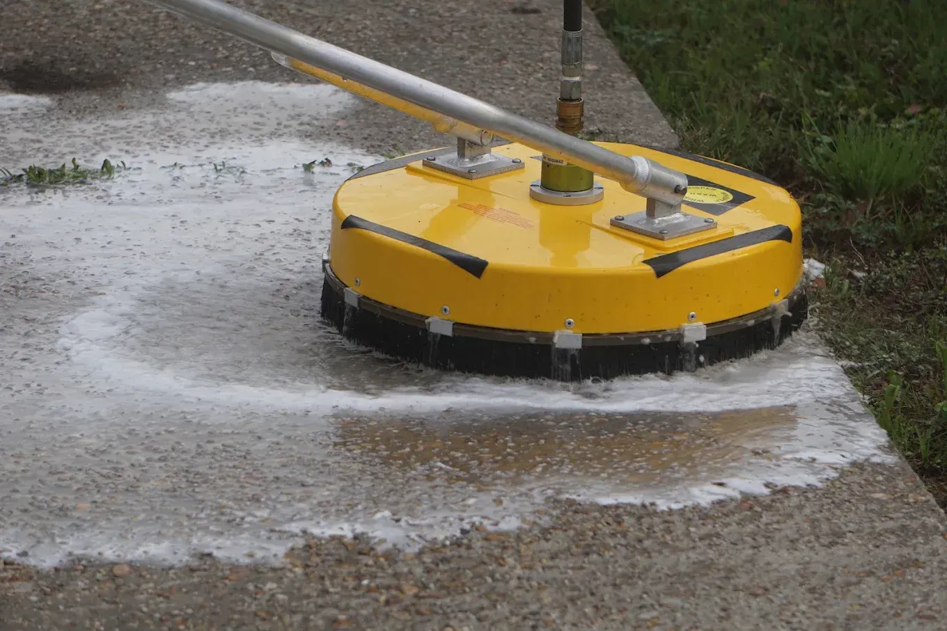 Yellow pressure washer cleaning a wet concrete surface outdoors