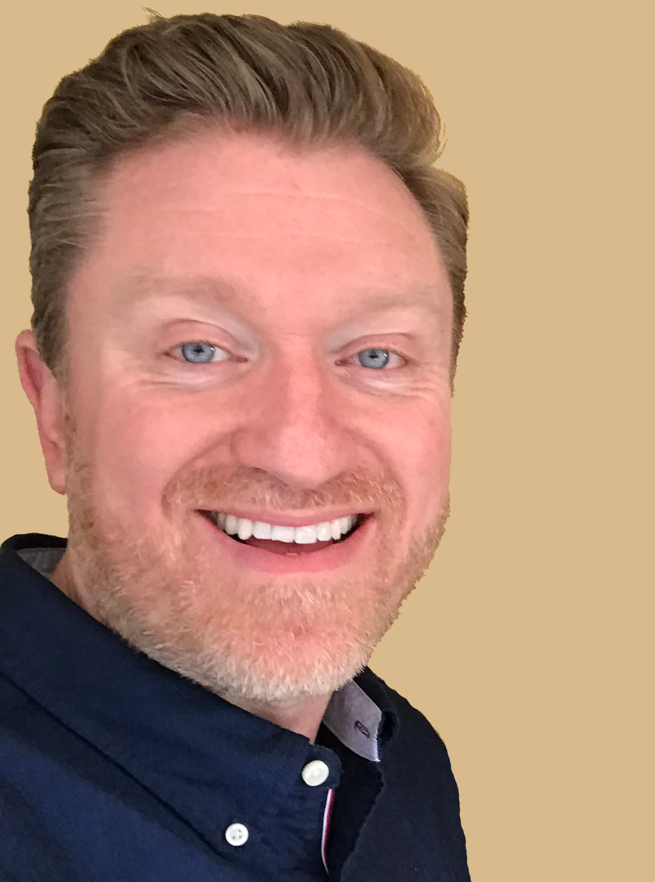 Man with blonde hair smiles, wearing a red collared shirt, against a gray background.