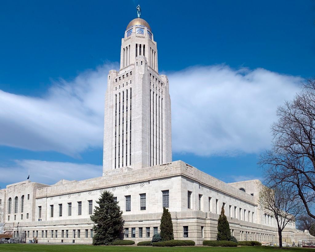 Nebraska State Capitol Building, a tall white tower with a gold dome, against a blue sky.
