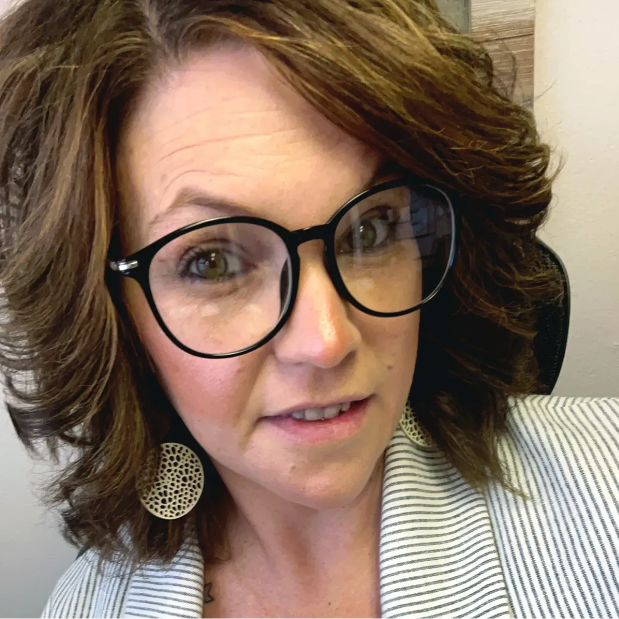 Woman with glasses and dark hair, wearing a striped blazer, looking at the camera.
