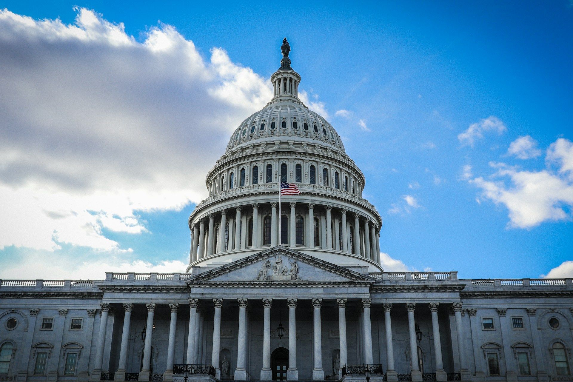 U.S. Capitol Building with white pillars and a large dome under a cloudy blue sky.