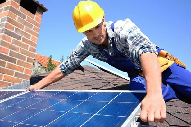 A Man Wearing a Hard Hat is Installing Solar Panels on a Roof — Spot On Solar International in Beresfield, NSW