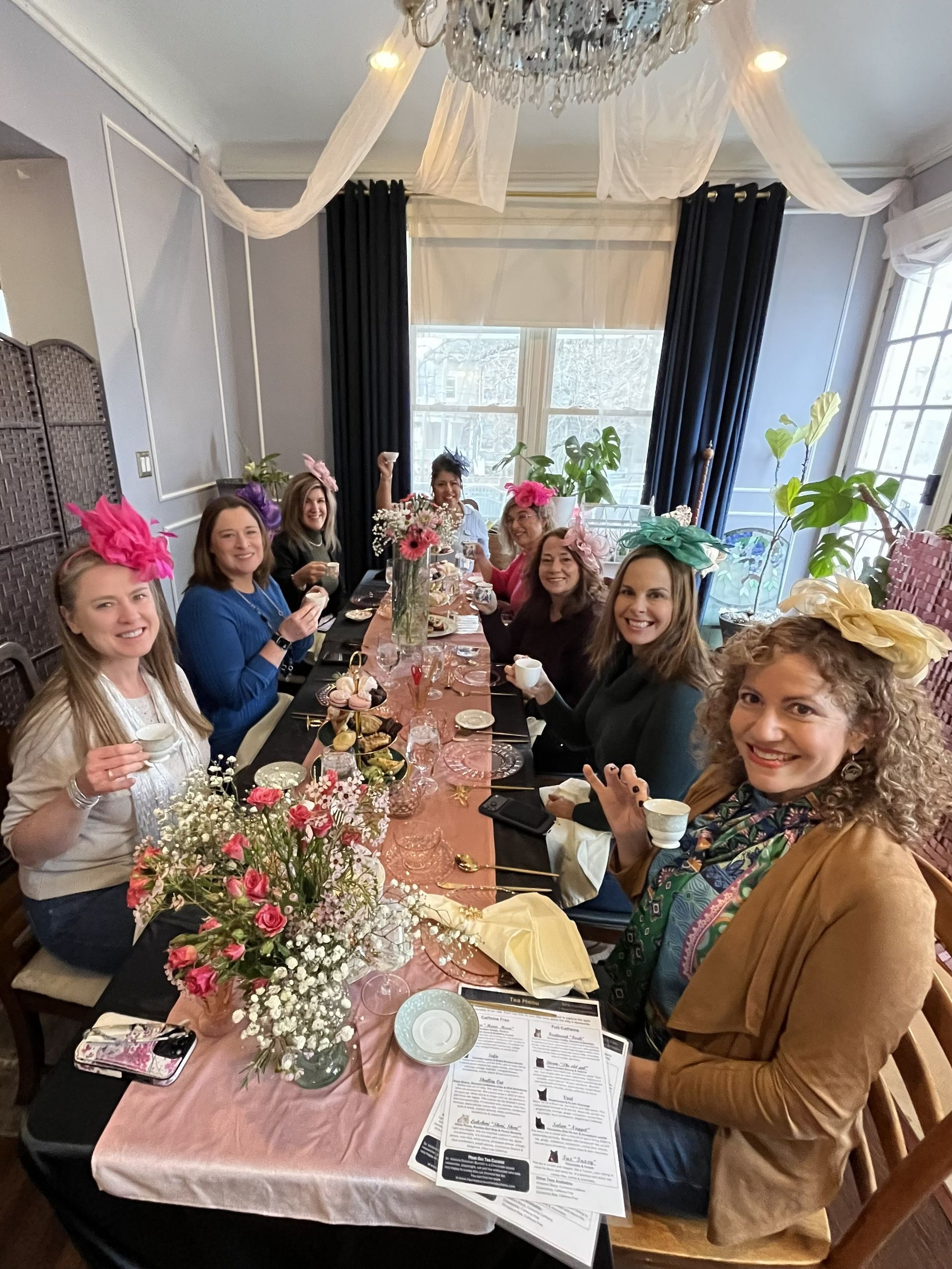 Six people smiling around a decorated table with flowers in a bright room with draped ceiling fabric