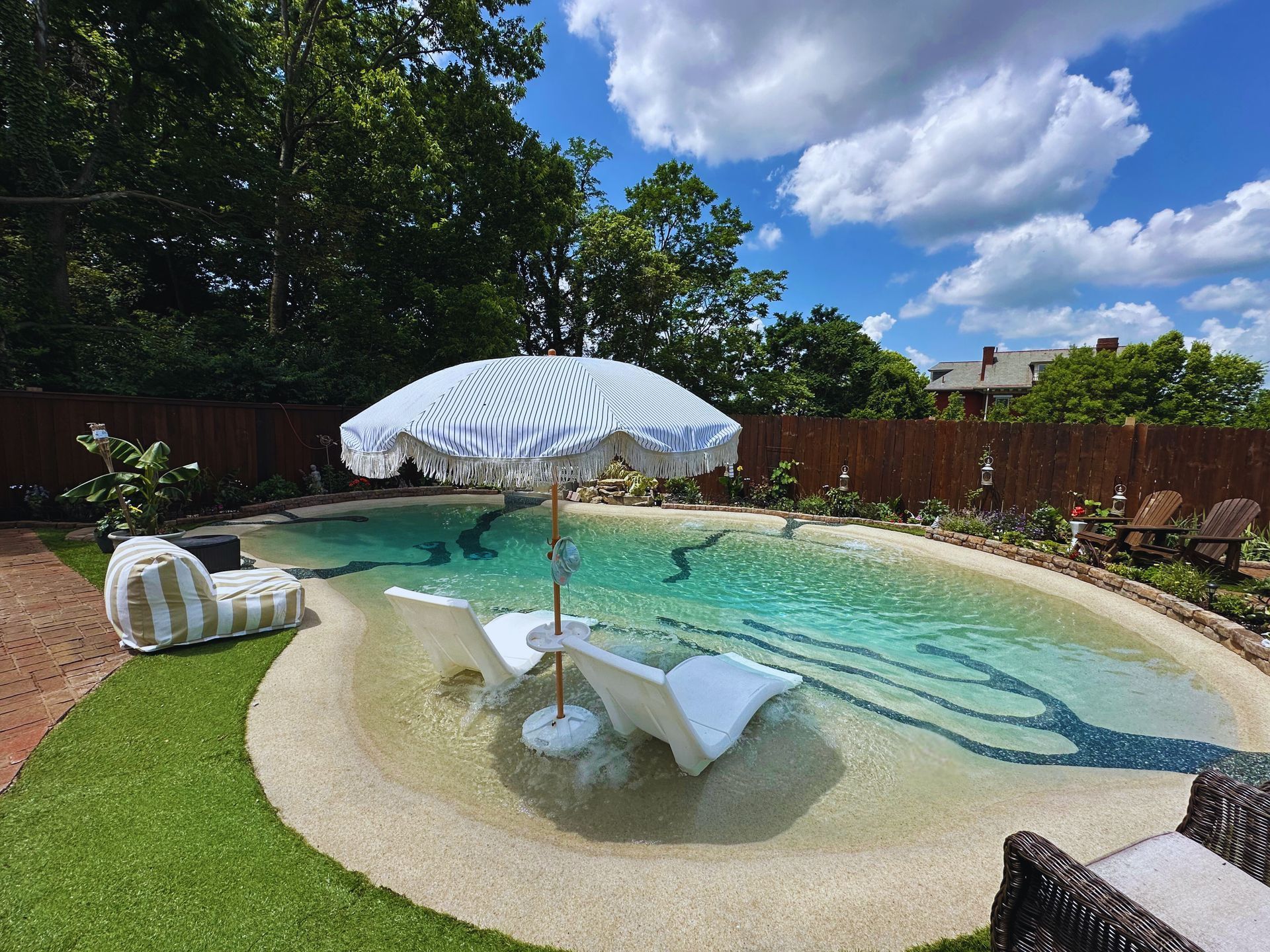 Backyard pool with a beach entry, lounge chairs, and a white umbrella.