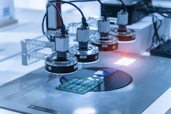 Automated lab machine inspecting a circuit board on a white workbench