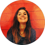 Woman with brown hair smiles in front of a red wooden wall.