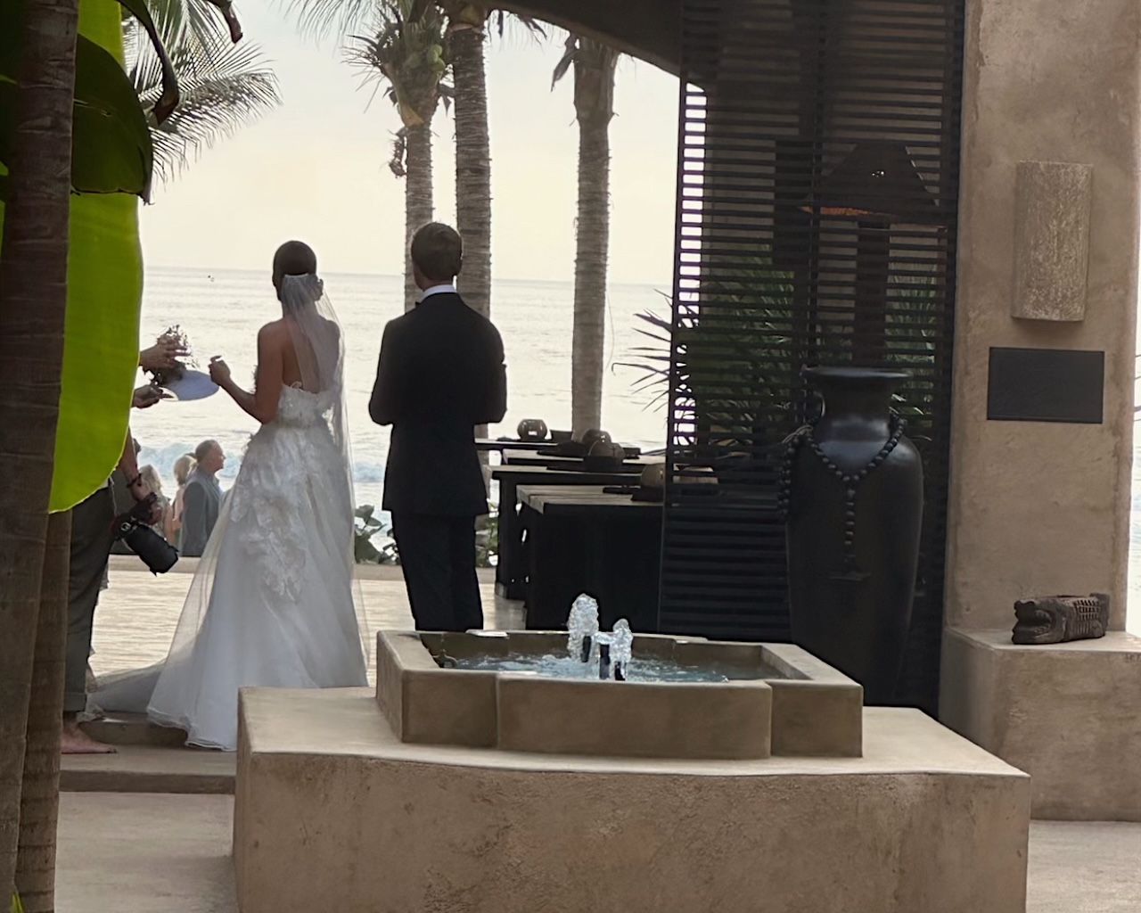A bride and groom are standing in front of a fountain