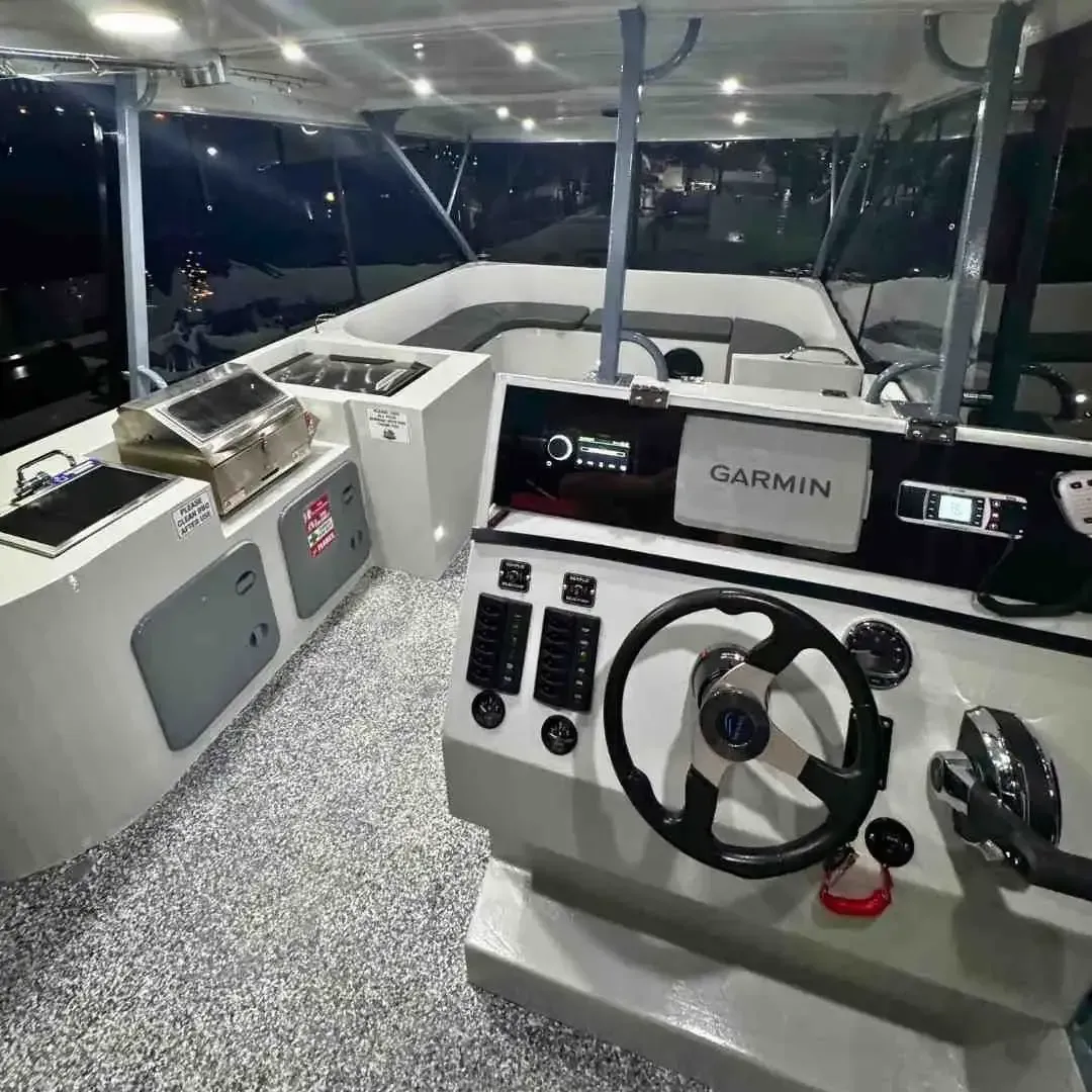 Boat's cockpit with gray and white interior. A steering wheel, Garmin display, grill, and seating are visible.