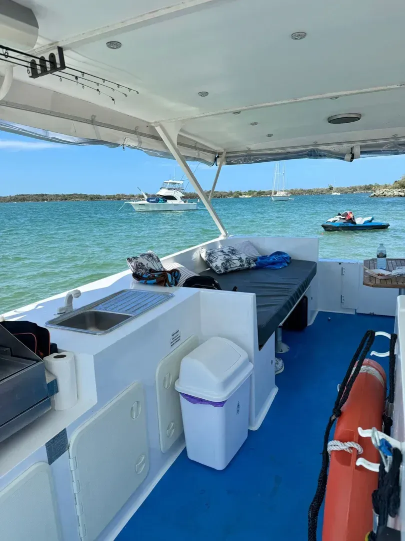 Interior of a pontoon party boat showing the kitchenette, BBQ, lounge seating, and a view of other boats on the water - Boat tours Gold Coast
