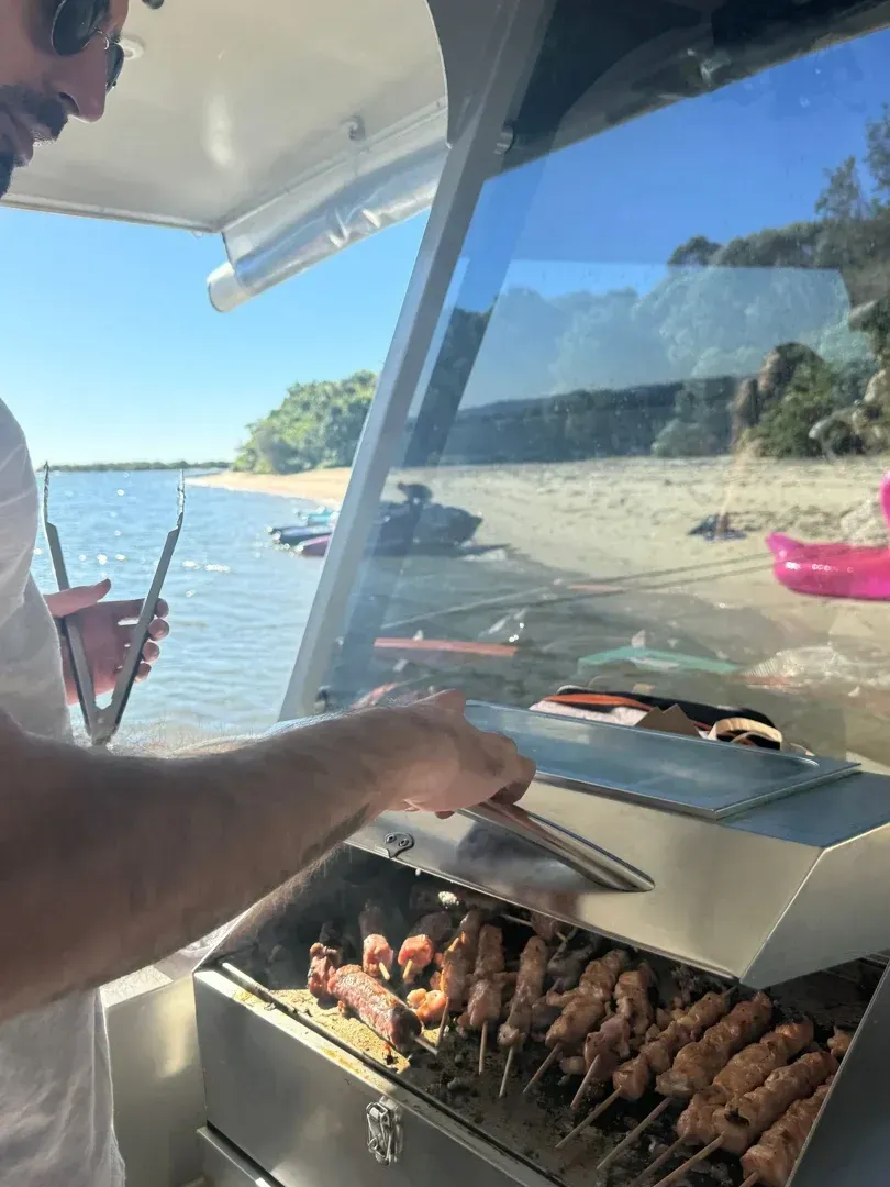 Gold Coast Marine Tours - A customer grilling BBQ sticks with the BBQ grill on the pontoon boat Gold Coast Marine Tours - A customer grilling BBQ sticks with the BBQ grill on the pontoon boat