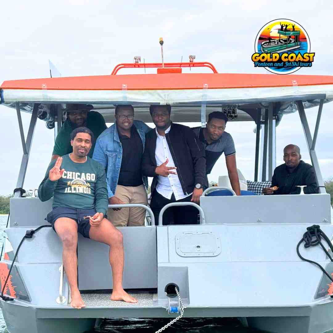 Group of men on a Gold Coast boat, posing for a photo, some smiling, water visible, bright sky.