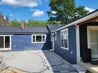 Blue house exterior with white trim, paved patio, and clear sky