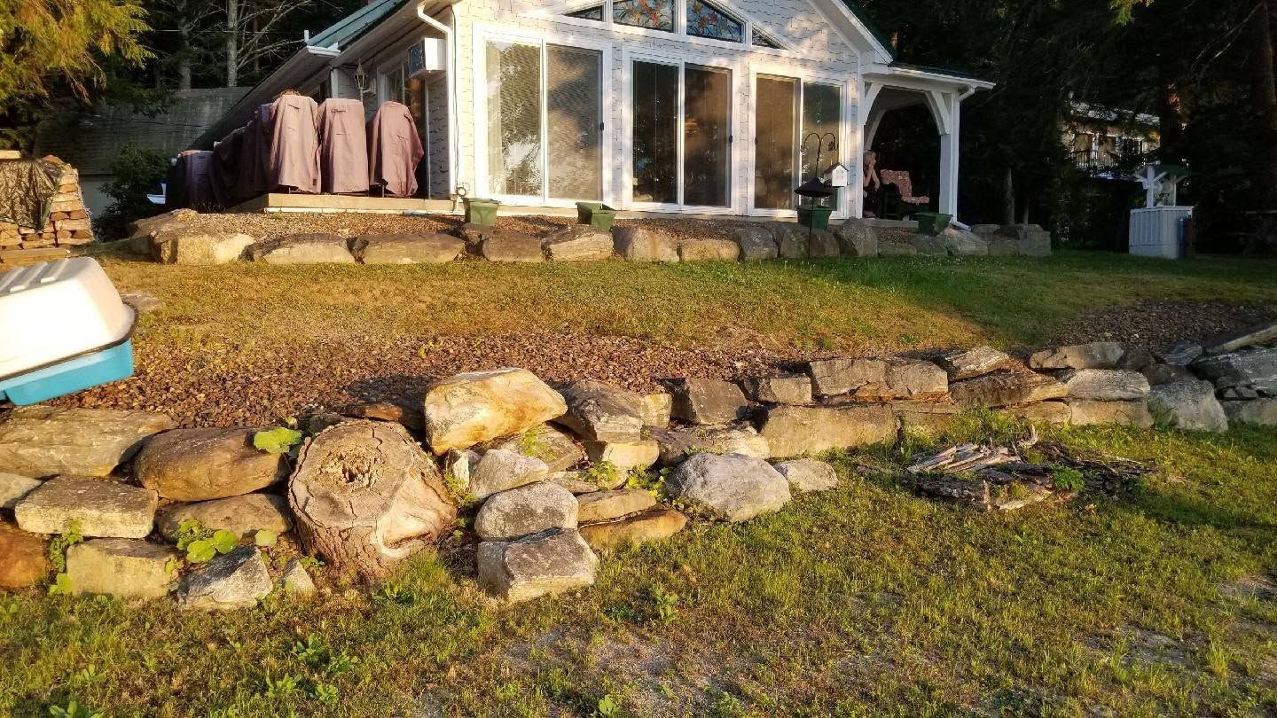 Rock garden in front of a small greenhouse with stacked stones and a grassy yard at sunset