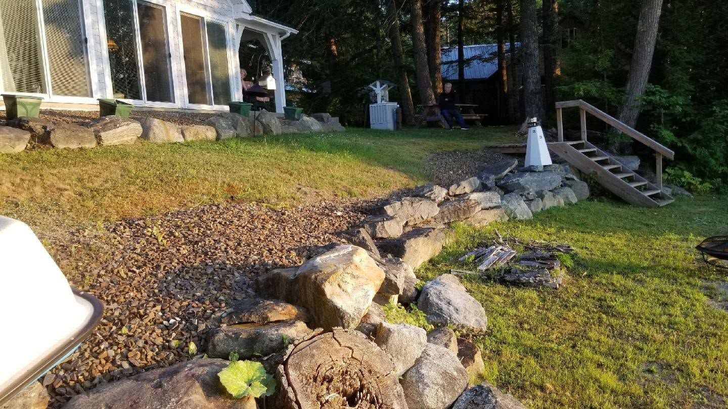 Rocky garden slope beside a house with porch, wooden steps, and scattered leaves in sunlight
