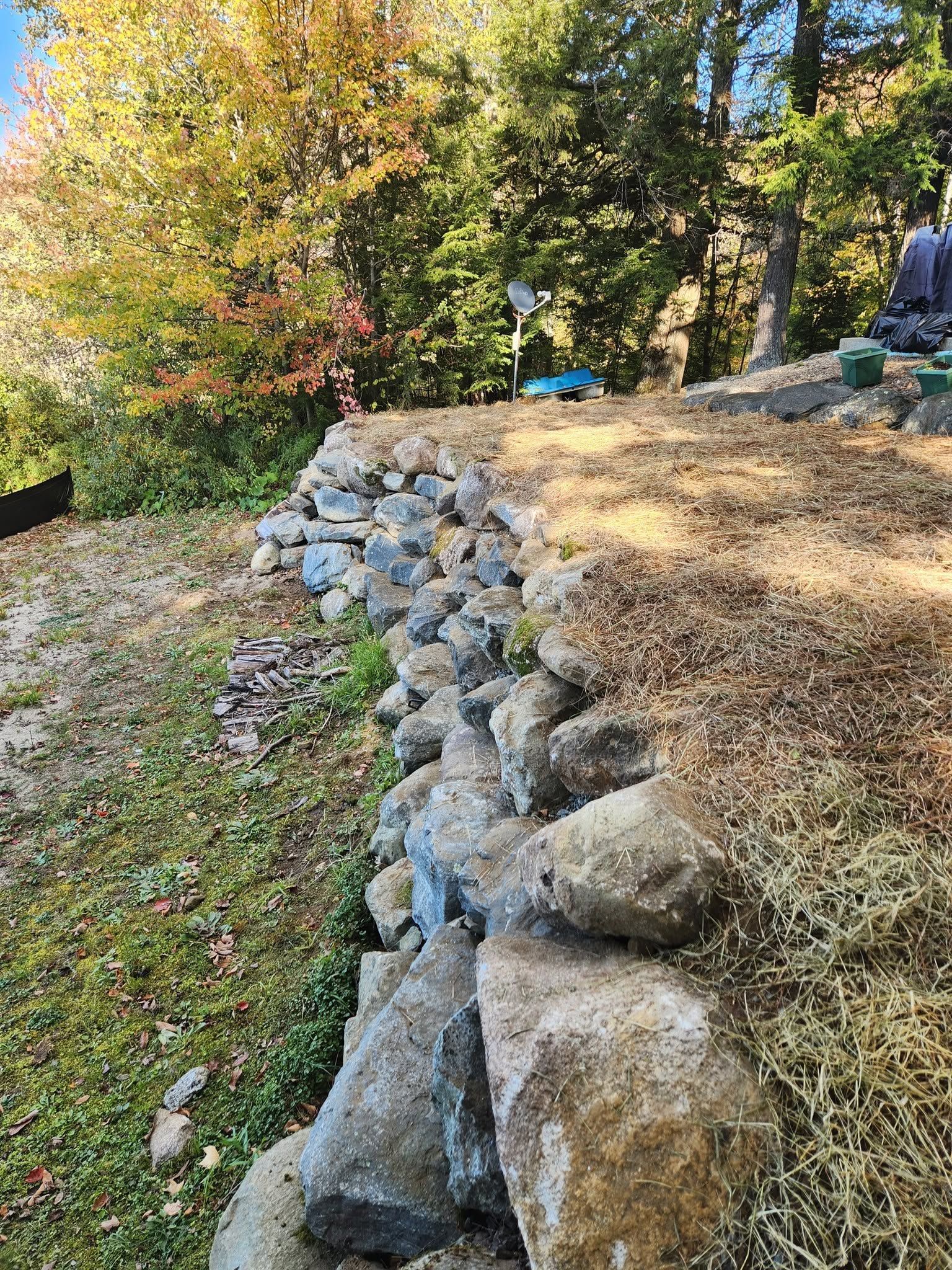 Rock retaining wall lining a grassy yard beside autumn trees and a gravel path.