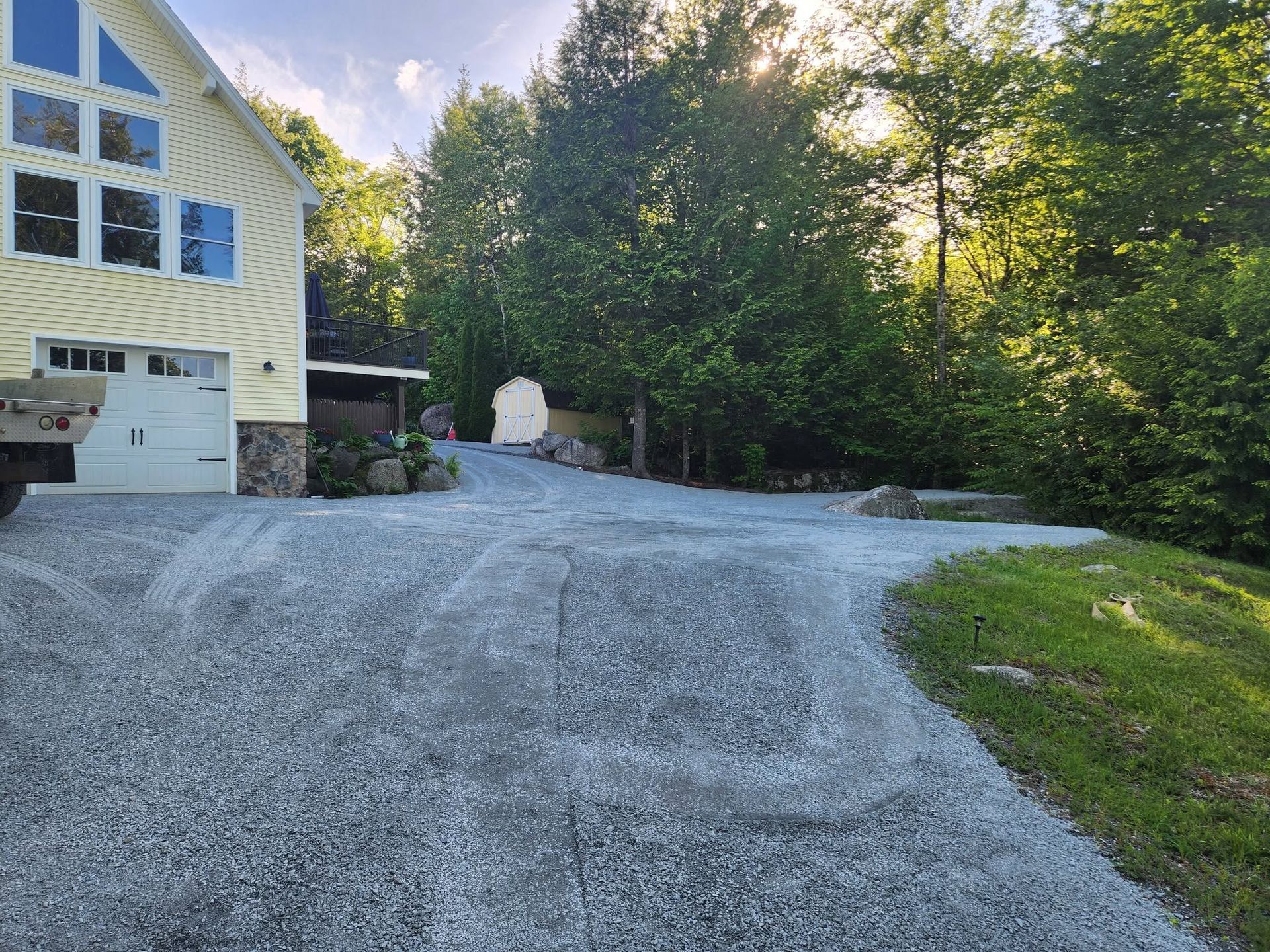Gravel driveway beside a yellow house, lined with trees and grass in late afternoon light.