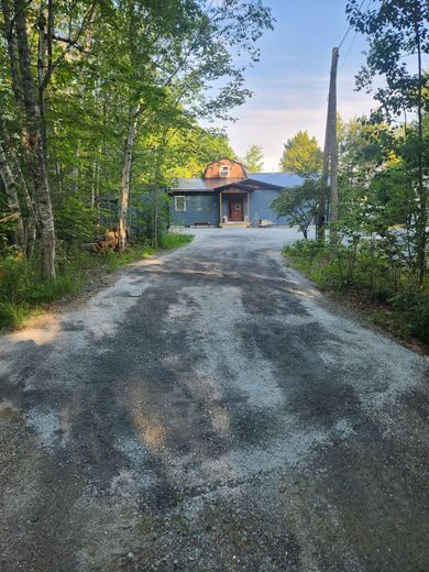 Gravel driveway leading to a cabin in a wooded area at sunset