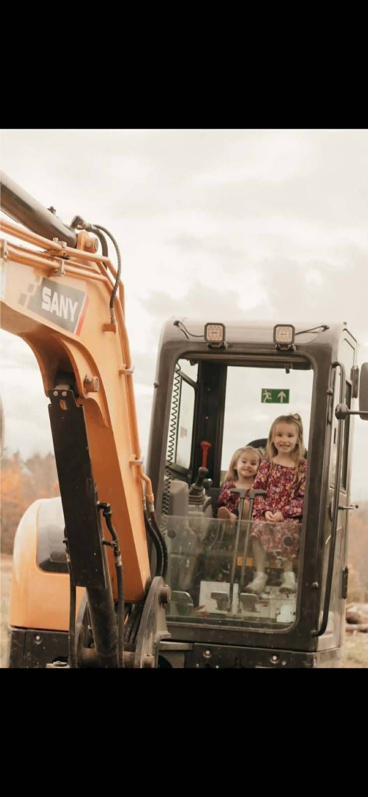 Excavator cab with a smiling person inside at a muddy work site