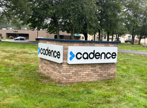 A sign for cadence is sitting in the grass in front of a building.