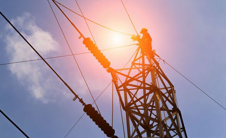 A man is standing on top of a power tower. 