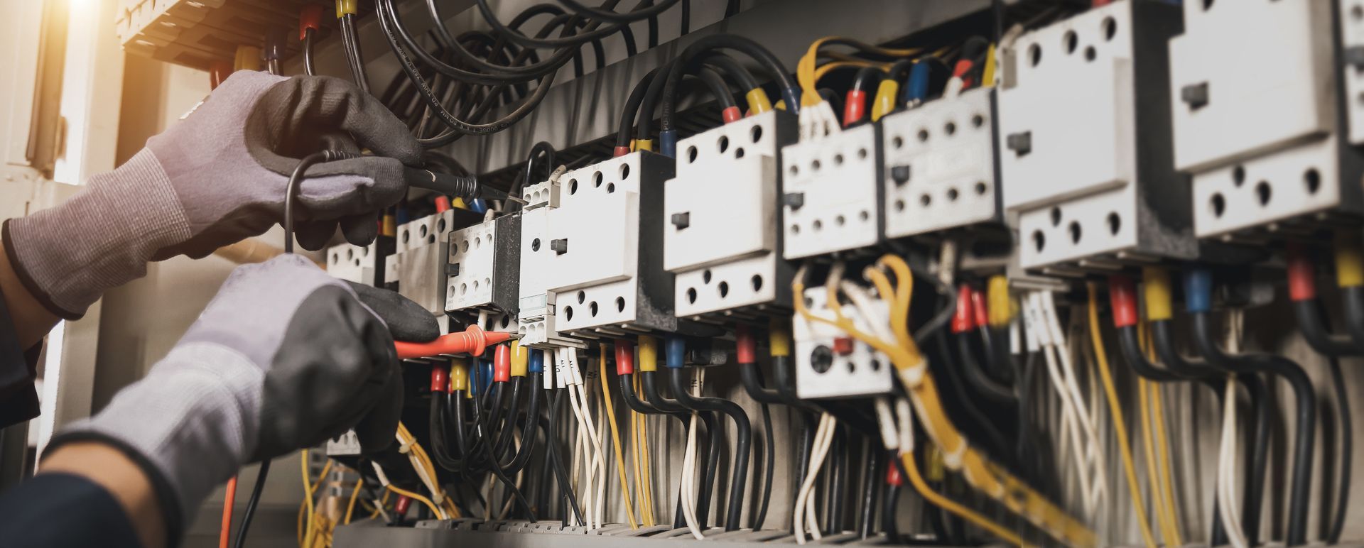 An electrician's hands wearing gloves working on a complex electrical panel. An electrician's hands wearing gloves working on a complex electrical panel.