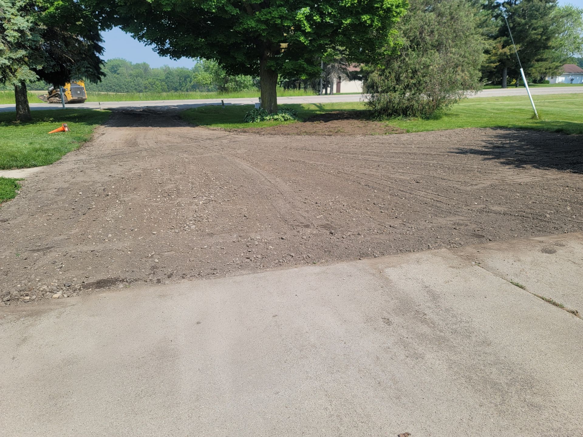 A gravel driveway transition extending from a paved surface toward a grassy yard with trees.
