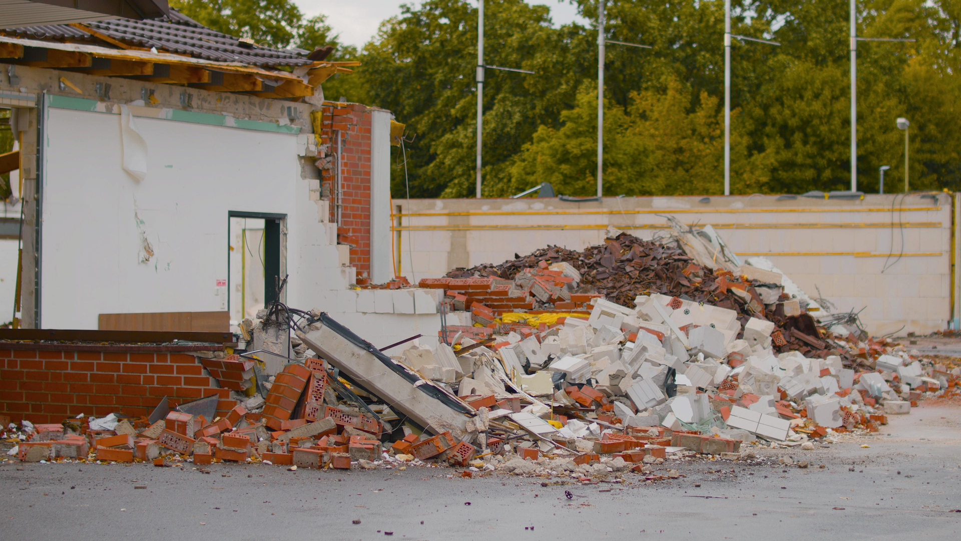 A pile of red brick and white concrete rubble sits in front of the partial remains of a demolished building.