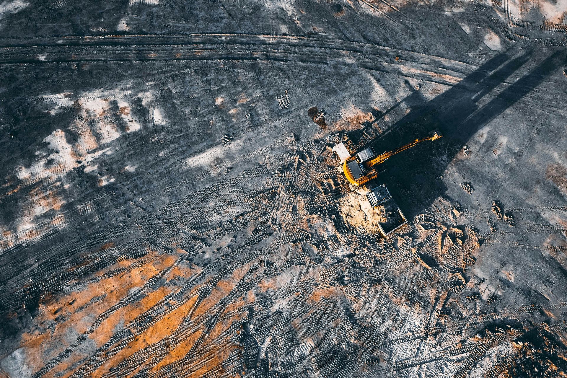 An aerial view of a yellow bulldozer clearing dark, rocky soil in an open-pit mine.