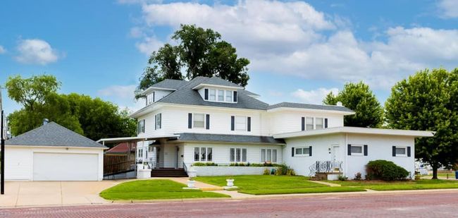 Large white house with wraparound porch, detached garage, and green lawn under a blue sky