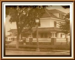 Sepia-toned photo of a large Victorian house behind a tree and front fence