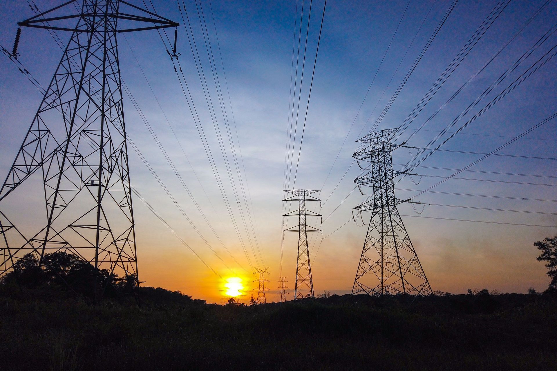Sunset behind power lines and transmission towers over a dark field