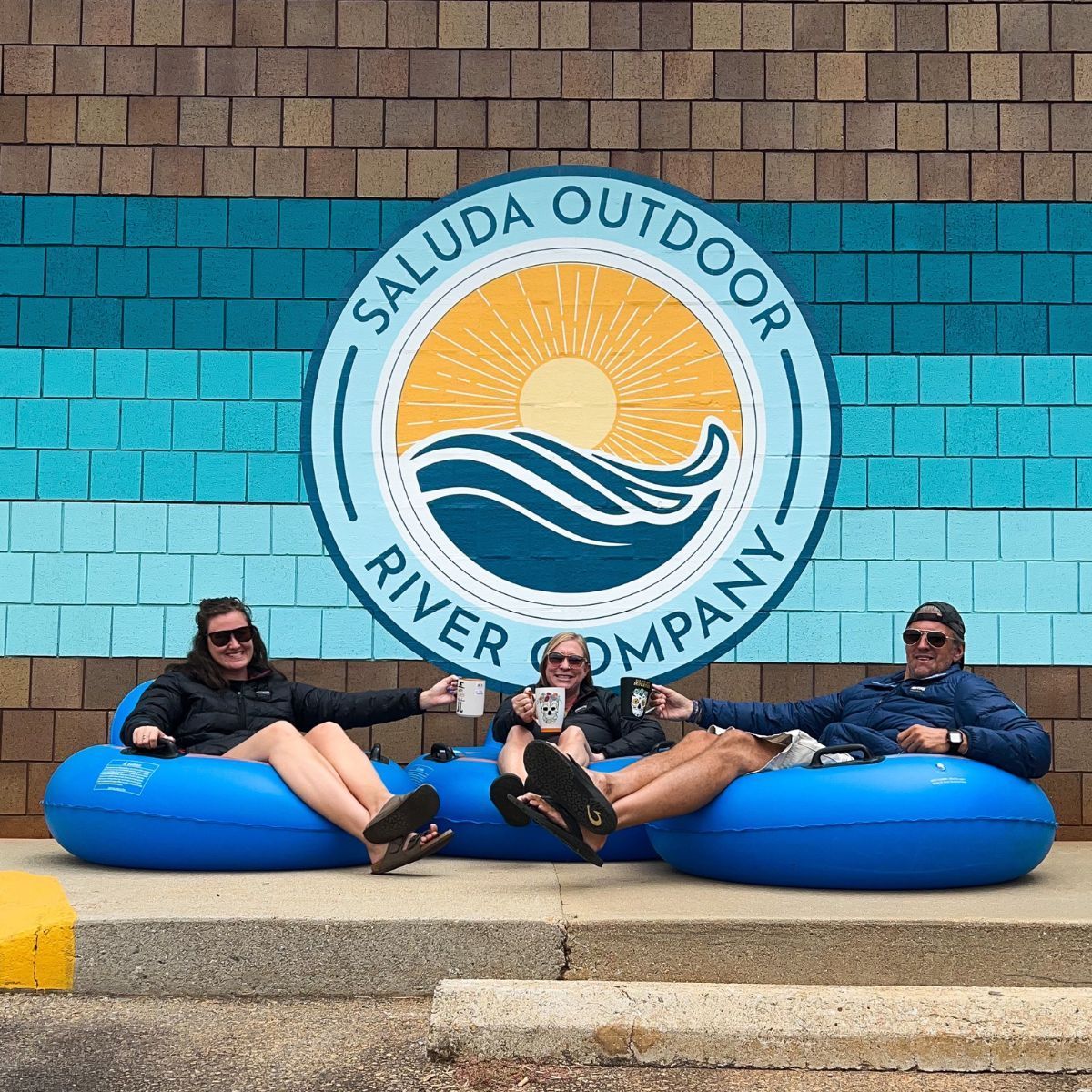 Three happy tubers in front of the Saluda Outdoor River Company mural.