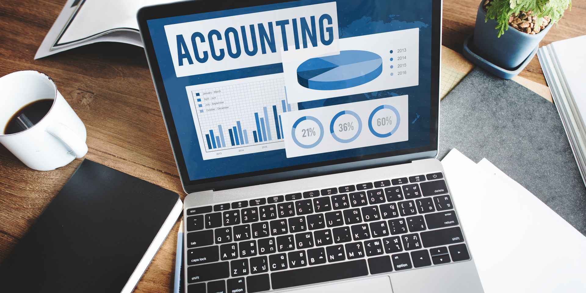 Laptop displaying accounting data with graphs, surrounded by a coffee cup, notepad, and papers on a wooden desk.