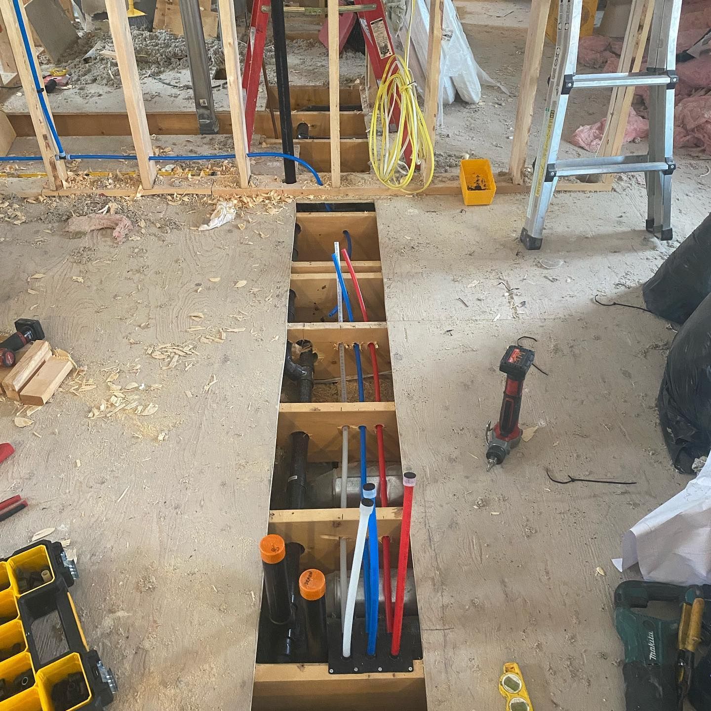 A wooden rectangular frame set in a floor, containing multiple colorful PEX plumbing pipes at a residential construction site.