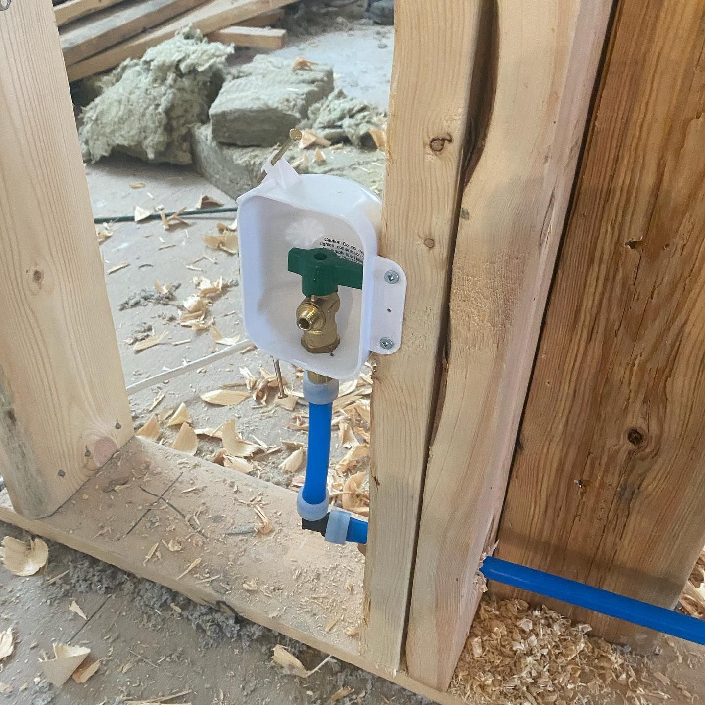 A PEX blue water pipe with a green-handled shut-off valve installed in a white plastic box on a wooden wall frame.