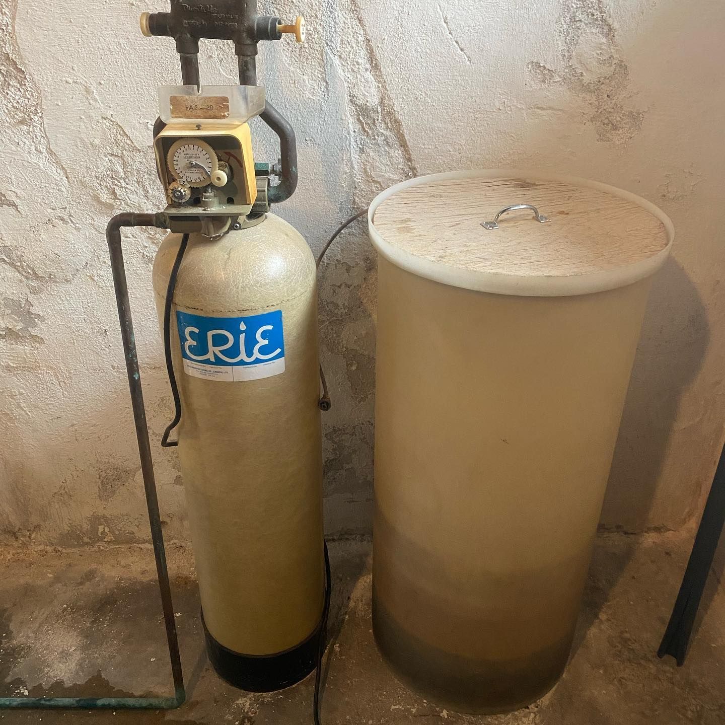 A beige Erie water softener tank standing next to a matching cylindrical brine tank against a concrete wall.