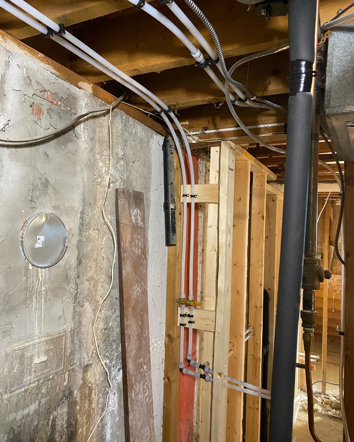 Exposed basement joists with PEX plumbing lines running along a wooden stud wall next to a concrete foundation.