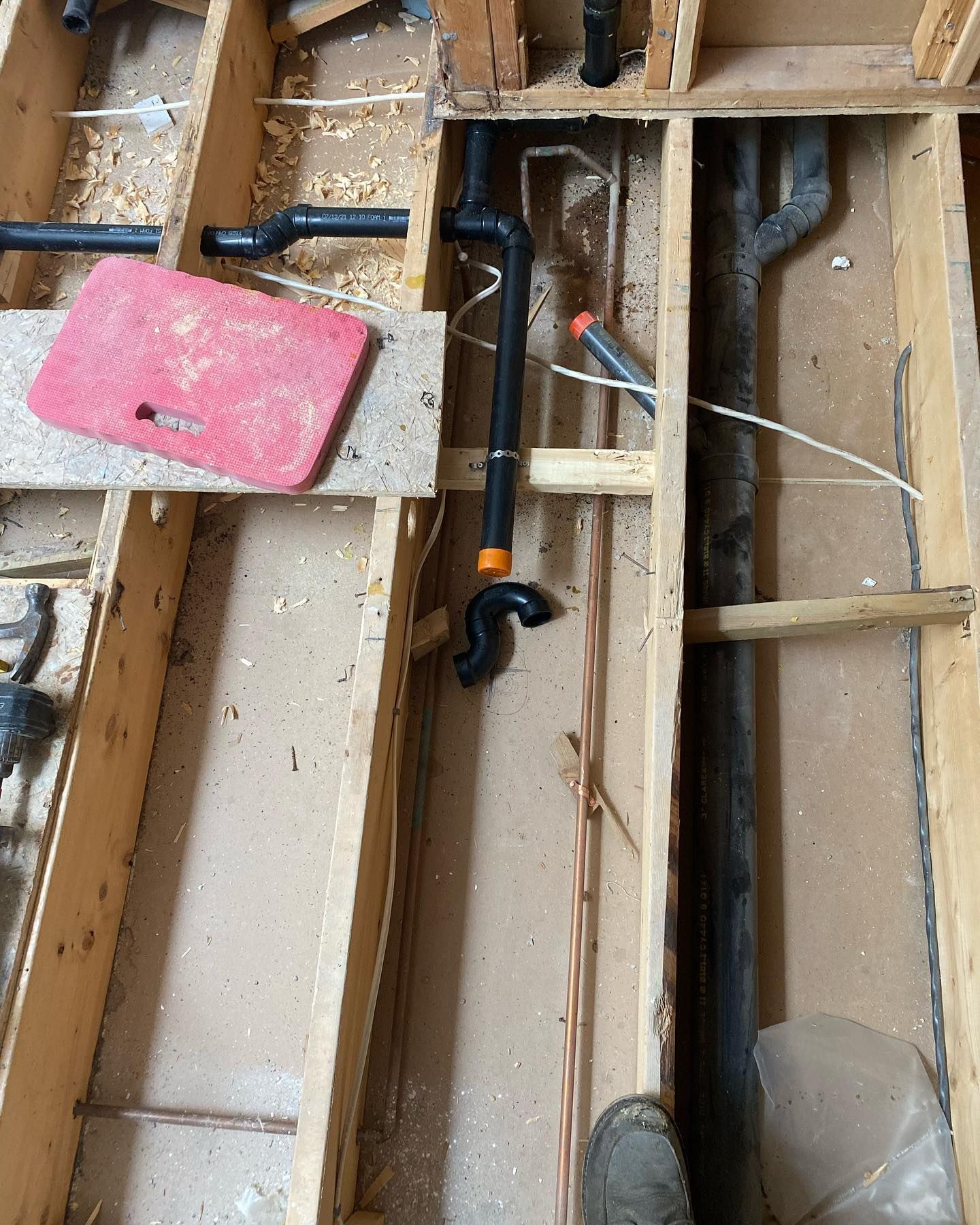 An overhead view of plumbing pipes and P-traps being installed between exposed wooden floor joists during construction.