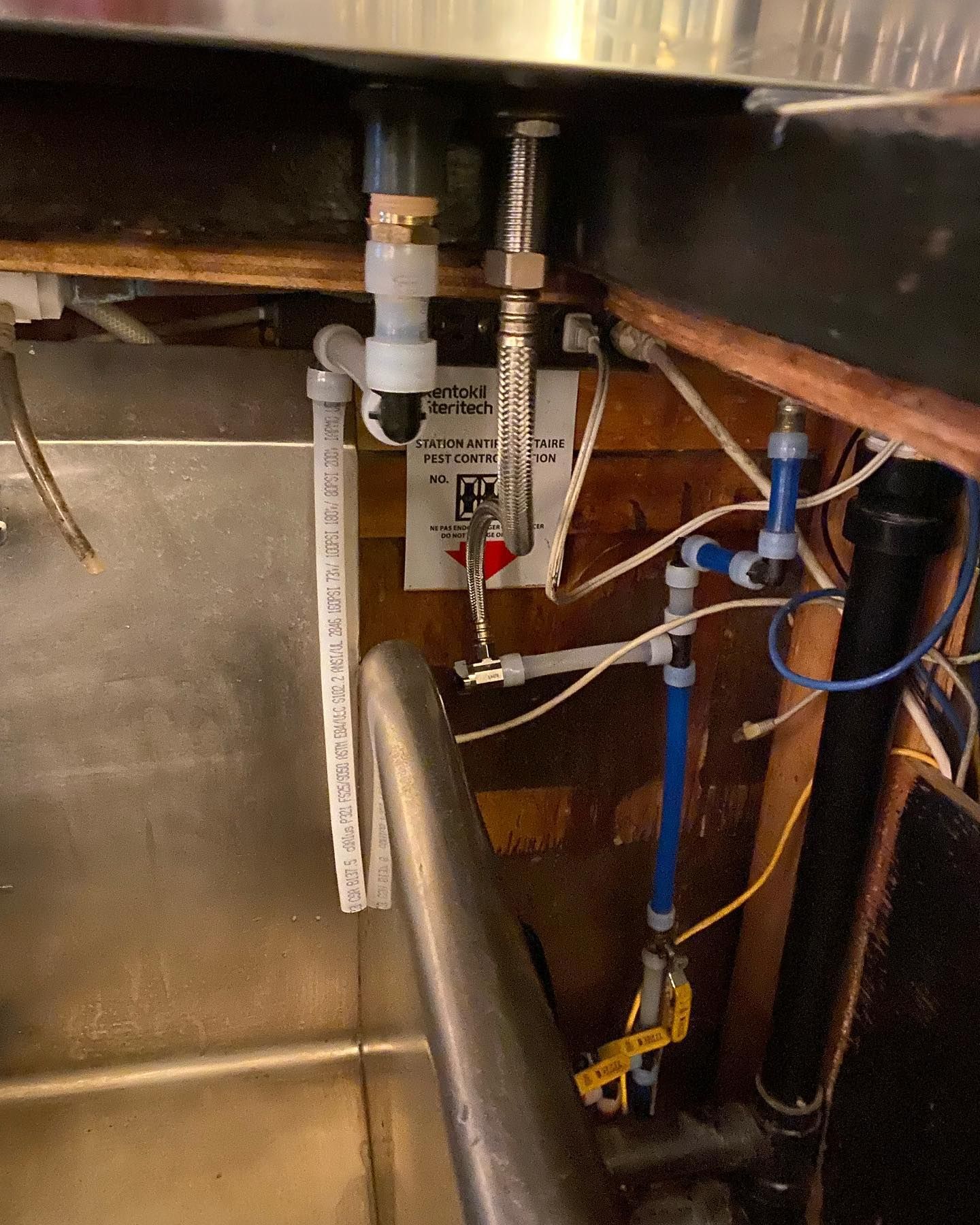 A close-up view under a sink showing plumbing pipes, flexible hoses, and shut-off valves connected to the faucet.