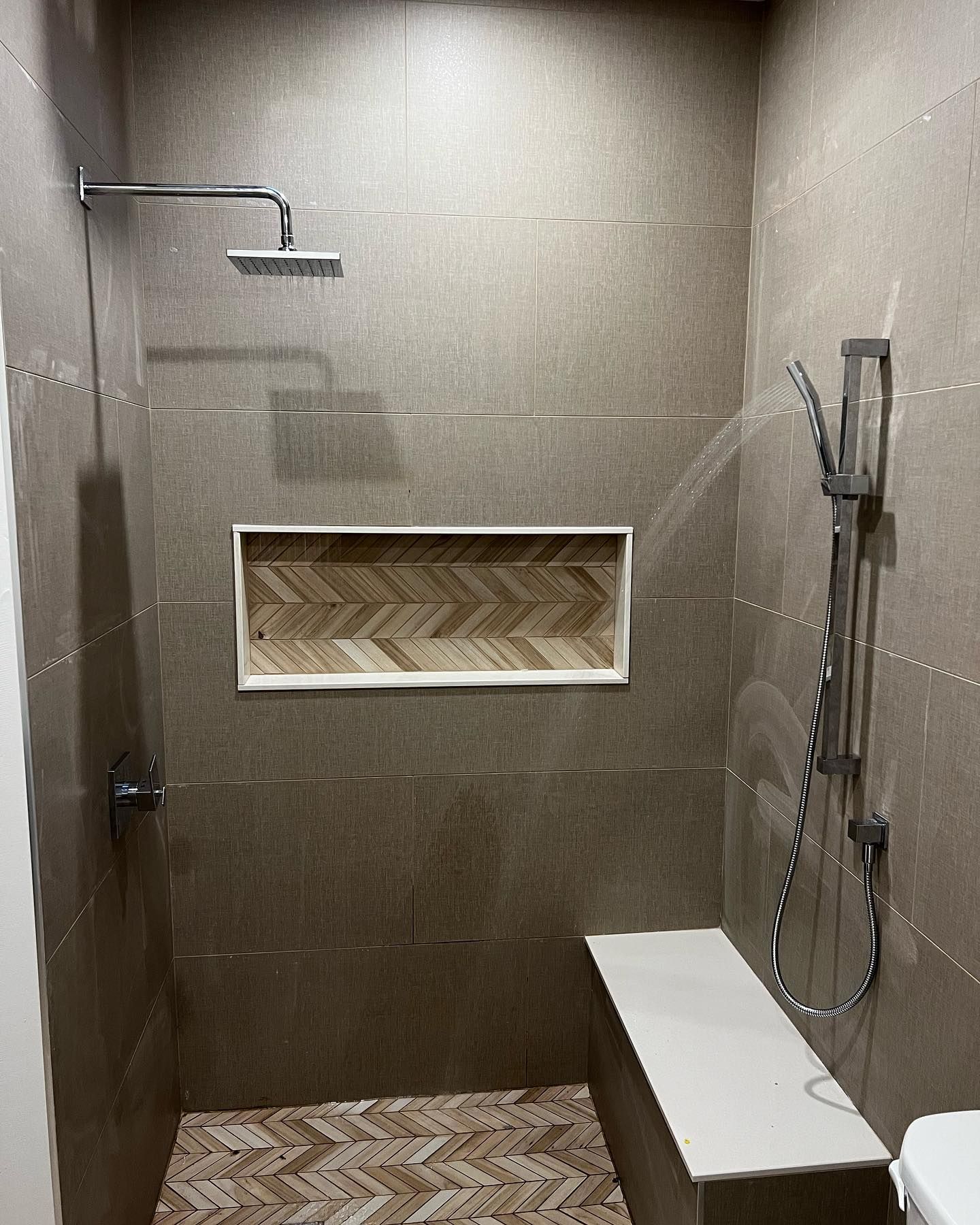 A tiled walk-in shower with a rainfall showerhead, handheld sprayer, built-in bench, and a chevron-patterned wall niche.