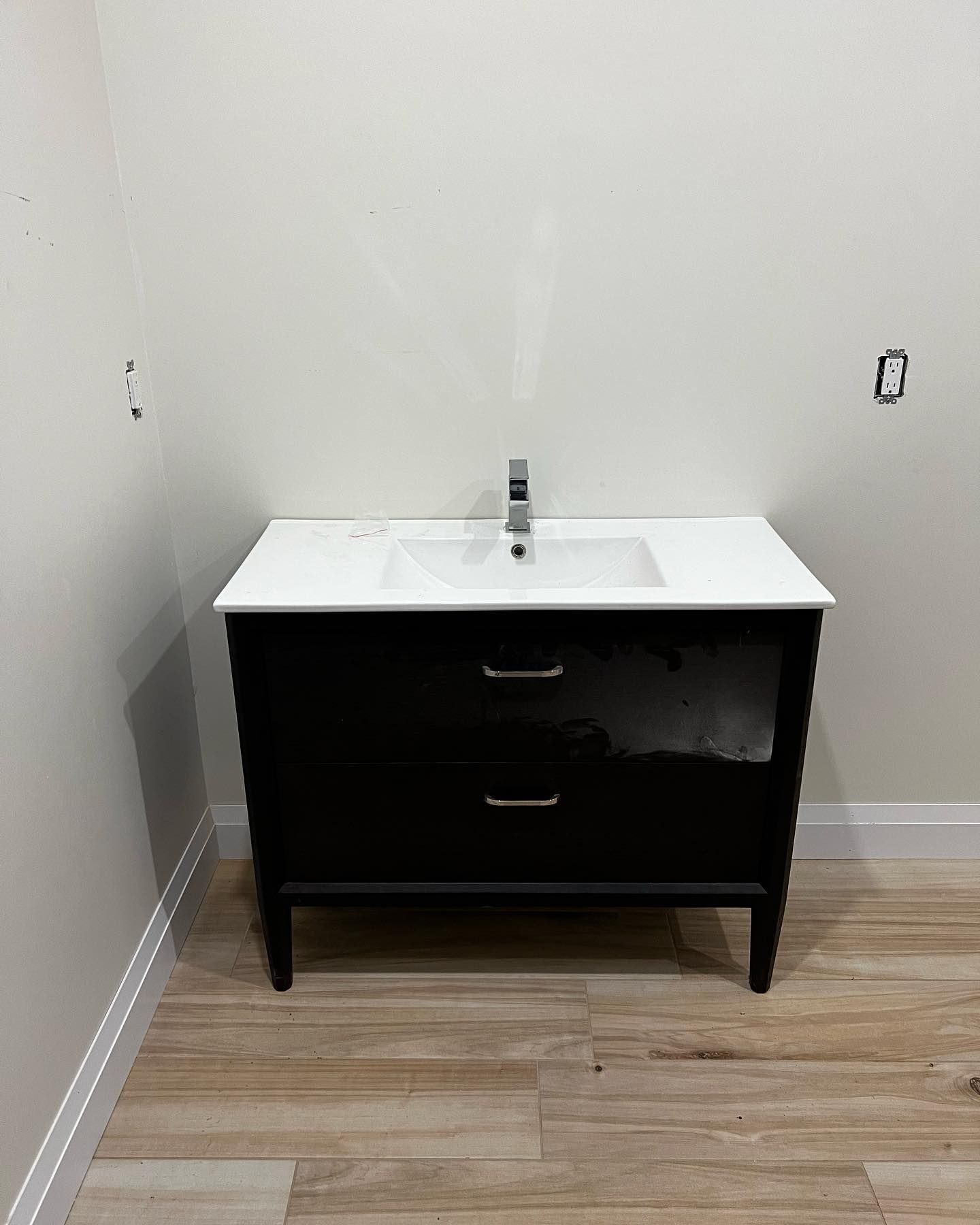 A modern black vanity with two drawers and a white countertop with a single faucet, centered against a plain white wall.