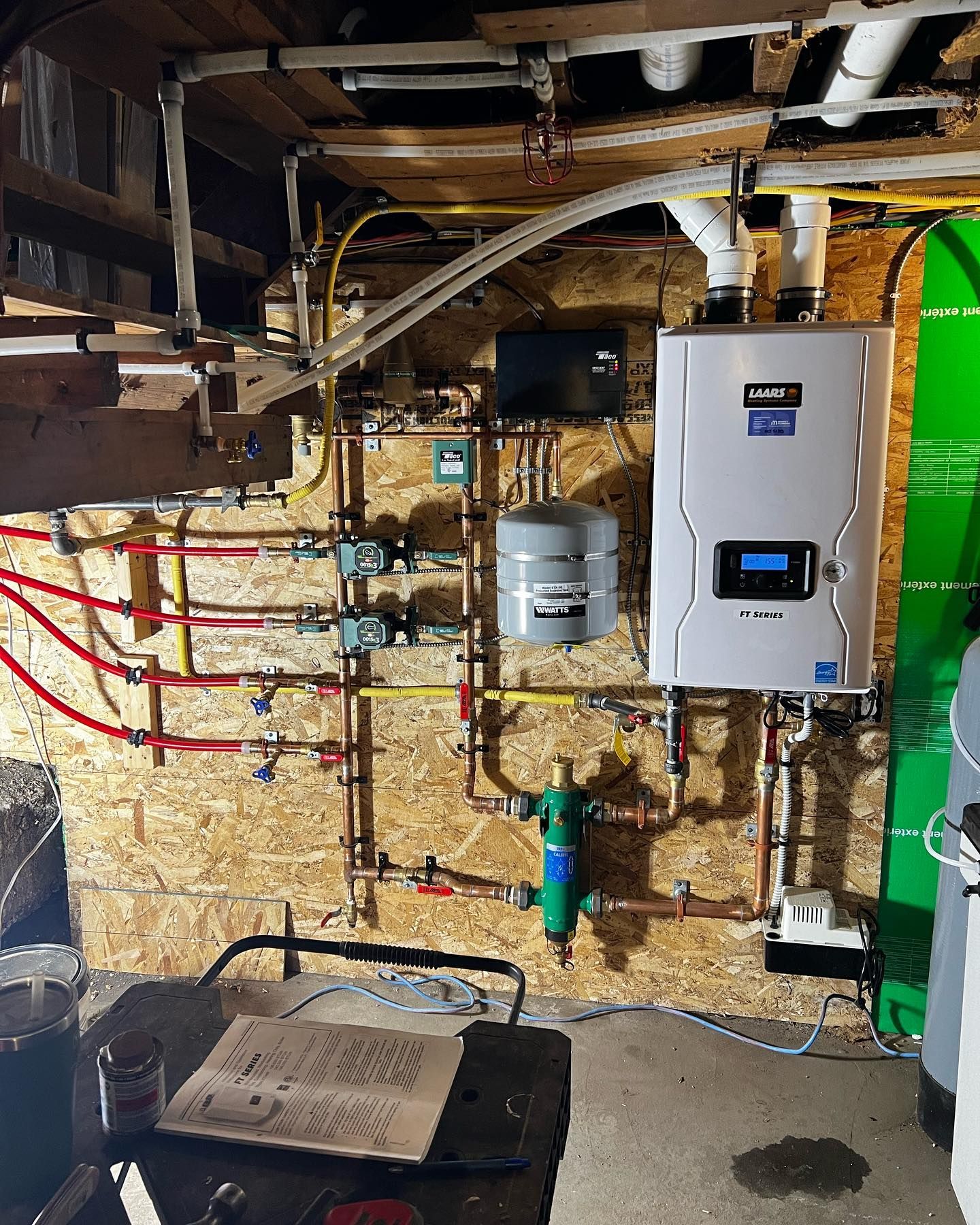 A Bosch wall-mounted boiler and pump system installed on a wooden wall in a basement mechanical area.