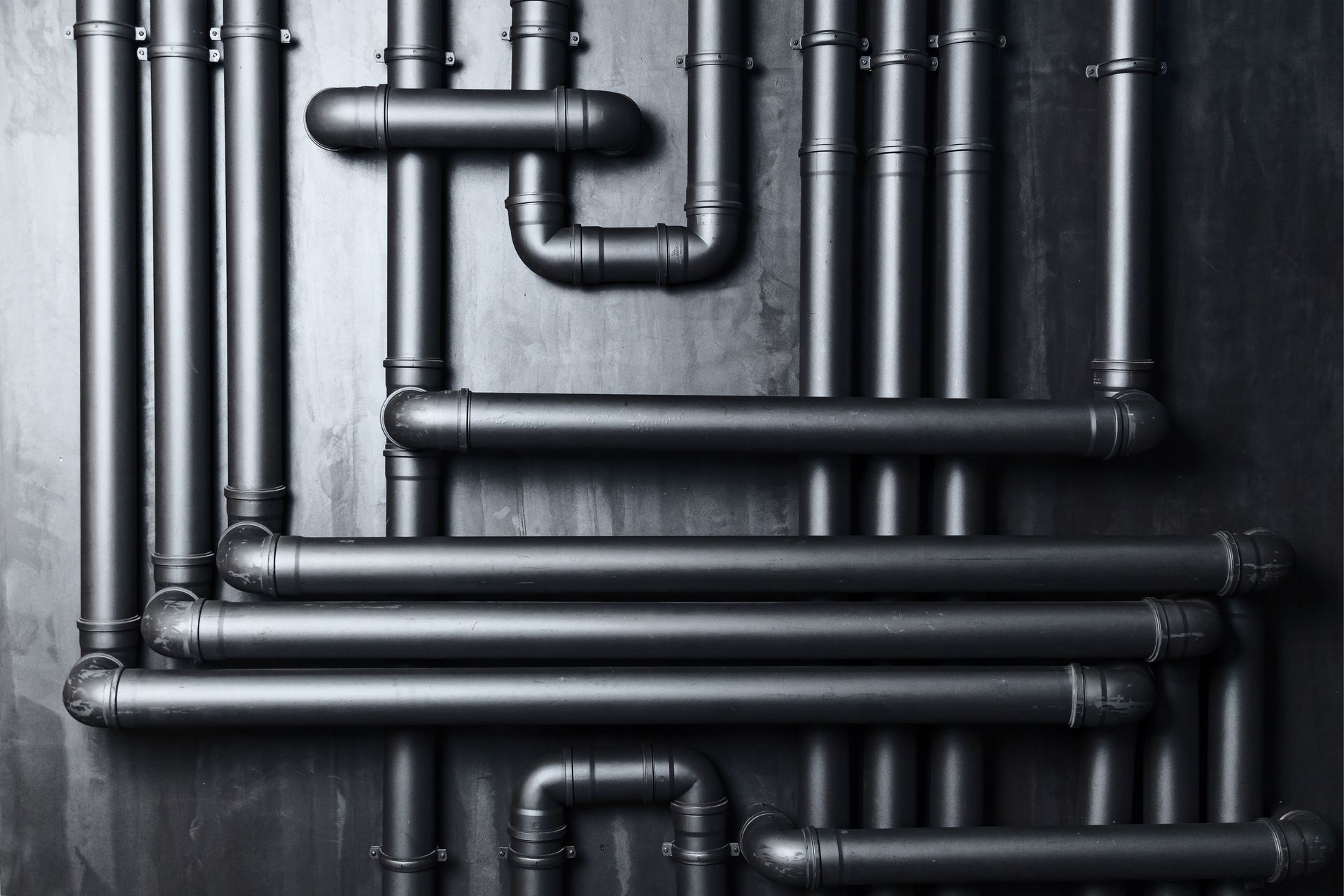 Black industrial pipes and elbows arranged on a dark wall background.