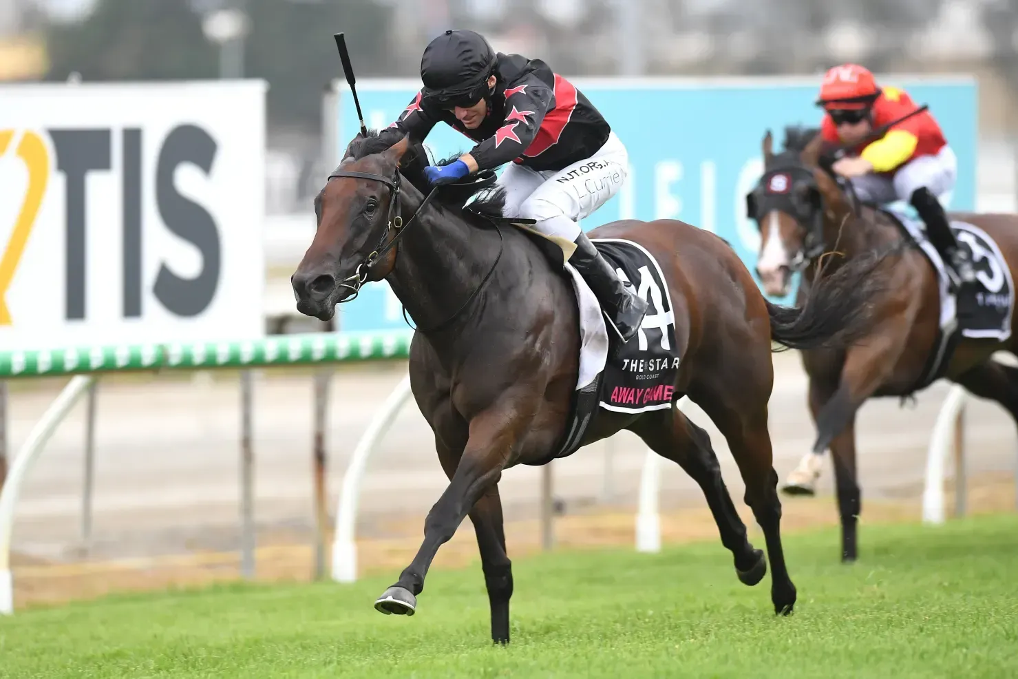 Two jockeys race dark horses on a wet track, with the front horse leading near the finish.