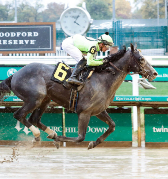 Two racehorses in a muddy track finish, with jockeys leaning forward and a clock in the background.
