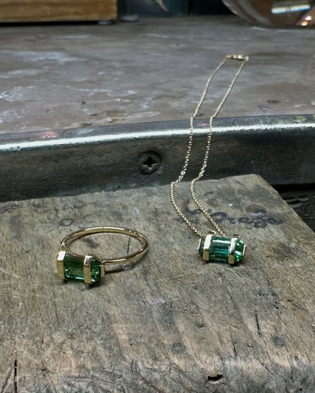Anello in oro e ciondolo abbinato con pietre verdi su una superficie di legno anticato.
