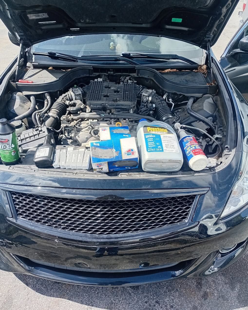 Open car hood with engine bay packed with assorted bottles and cans on the front grille.