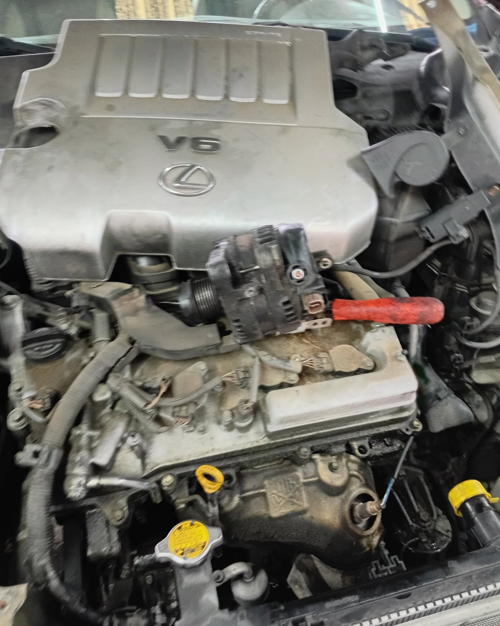 Lexus V6 engine bay with exposed components and red jumper cable clamp attached