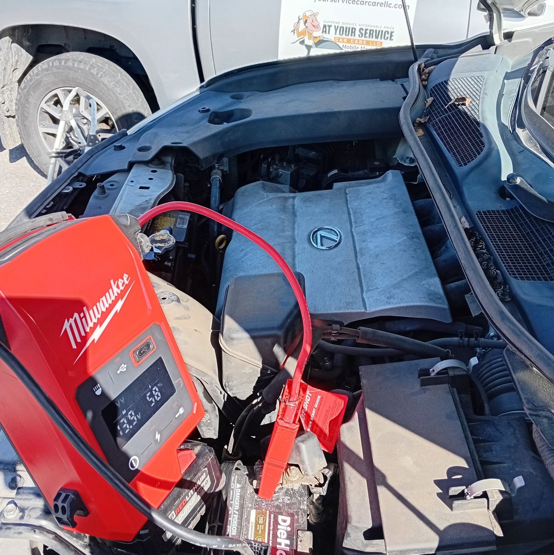 Jump-starting a car engine with a red Milwaukee battery charger under the open hood.