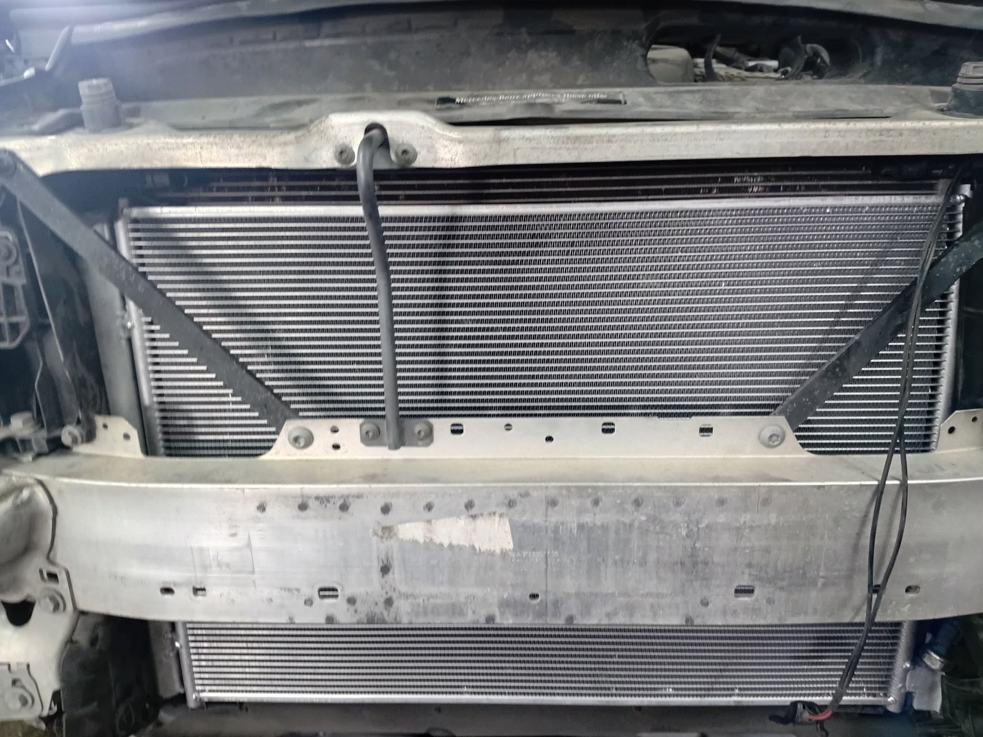 Car front with bumper removed, exposing radiator, condenser, and metal support frame